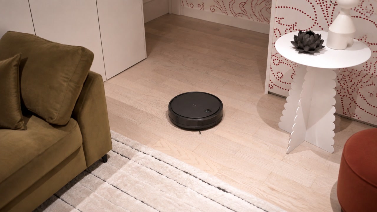 Робот-пылесос очищает светлый кварцевый паркет в интерьере гостиной